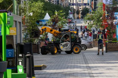 Quebec, Kanada, 06 Temmuz 2025: Yoğun şehir sokak festivali kurulumu sırasında işçi sarı inşaat aracı