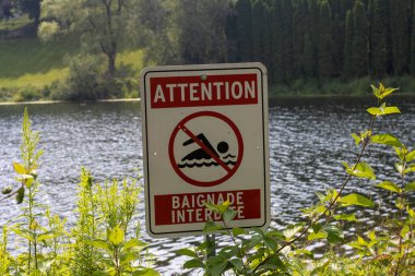 Kanada, 26 Temmuz 2025: Uyarı işareti sakin nehir suyu yakınında yüzme etkinliğini yasakladı.