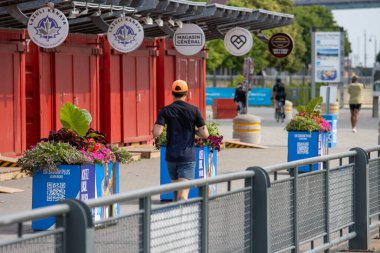 Quebec, Kanada, 05 Temmuz 2025: Turuncu şapkalı adam kırmızı kulübelerin ve çiçeklerin yanından geçiyor