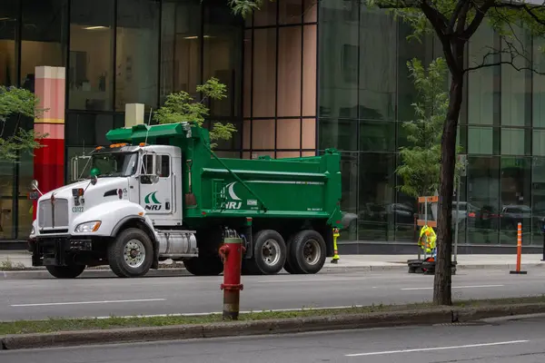 Kanada, 07 Temmuz 2025: İşçi yakınındaki cam binanın yakınına park edilmiş yeşil inşaat kamyonu
