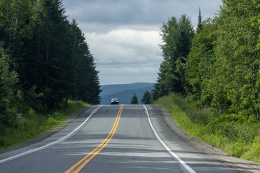 Quebec, Kanada, 20 Temmuz 2025: Tek başına gezen araba yemyeşil yüksek ağaçlar arasında dolambaçlı yol