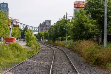 Quebec, Kanada, 05 Temmuz 2025: Ağaçların arasından uzak şehir binalarına doğru uzanan eğri tren yolu