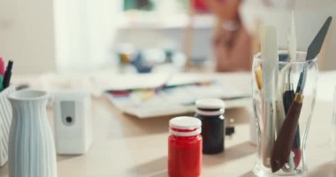 Ön plan boya ekipmanlarına yakından odaklan. Renkli su, yağlı ve akrilik fırça. Genç Asyalı kadın sanatçı, evdeki rahat atölyede resim yaparken önlük giyiyor. Yaratıcılık kavramı.