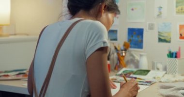 Genç Asyalı kadın önlük takıyor çizim defterine resim çiziyor geceleri evde rahat bir atölye çalışması yapıyor. Çağdaş Ressam Soyut Modern Sanat, Yaratıcılık ve İnsan Konsepti.