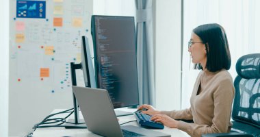 Genç yetişkin Asya kadın bağımsız gözlük yazma komut AI bot IT uygulama akıllı program göçebe, video oyunu, kodlama, kullanıcı arayüzü, tasarımcı, masaüstü bilgisayar büyük veri merkezi.