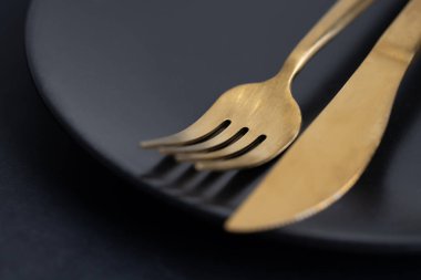 Golden cutlery on plate on dark background. Closeup. Eating concept. 