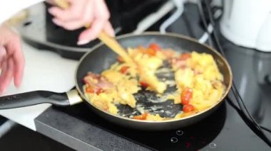 Ev yapımı omlet pişiren kadın. Mutfakta pastırma ve domates var.