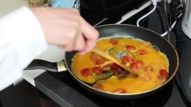 Ev yapımı omlet pişiren kadın. Mutfakta pastırma ve domates var.