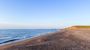Arkasında büyük beyaz bir kum bulunan deniz ve sahil manzarası.