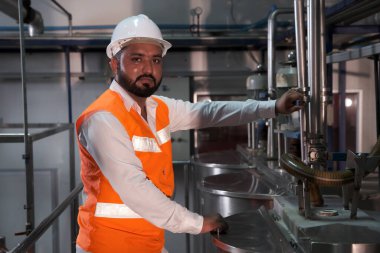 Asyalı erkek fabrika işçisi, insan mühendisi ya da uzman personel güvenlik yeleği ve bakım kaskı giyer ve buhar kazanını kontrol eder.