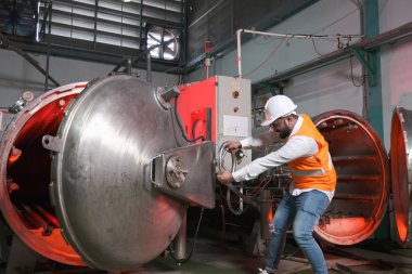 Güney Asyalı erkek fabrika işçisi veya mühendis veya uzman personel güvenlik yeleği ve bakım kaskı giyer ve buhar kazanını kontrol ederler.