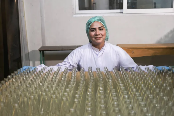 South asia senior woman factory worker or expert quality staff is checking bottles line for beverage