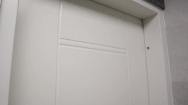Bu yakın plan video, projelerinize çağdaş zarafet katmak için mükemmel beyaz bir kapının üzerinde şık bir siyah kapı kolu sergiliyor. 5-20 saniyelik klip banyoda kullanmak için ideal.