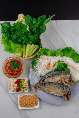 Kızarmış iki kısa gövdeli uskumru balığı ve beyaz tabakta sebze..