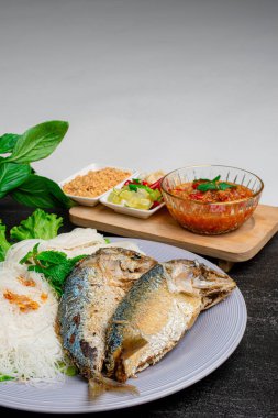 Kızarmış iki kısa gövdeli uskumru balığı ve beyaz tabakta sebze..