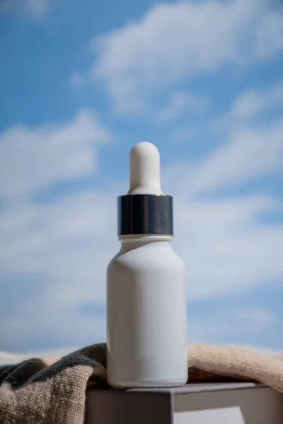 Gökyüzü arka planında beyaz bir cam damlası şişesi.