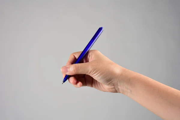 Close-up of a woman\'s hand holding a pen and writing gesture isolated on a grey background