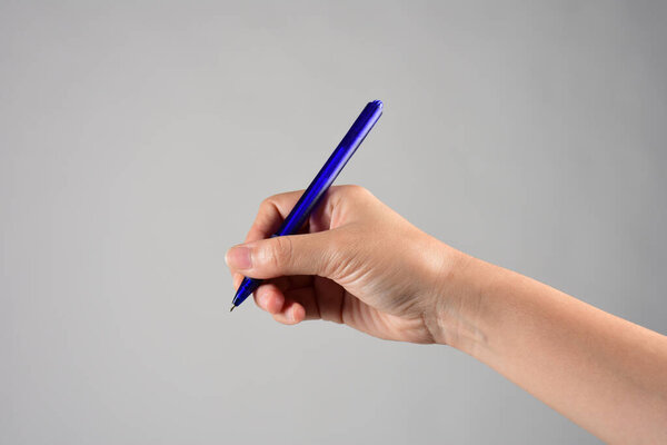 Close-up of a woman's hand holding a pen and writing gesture isolated on a grey background
