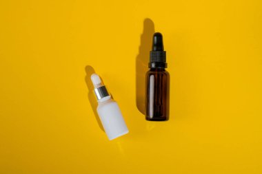 Sarı arka planda koyu kehribar camından yapılmış kozmetik şişeler..