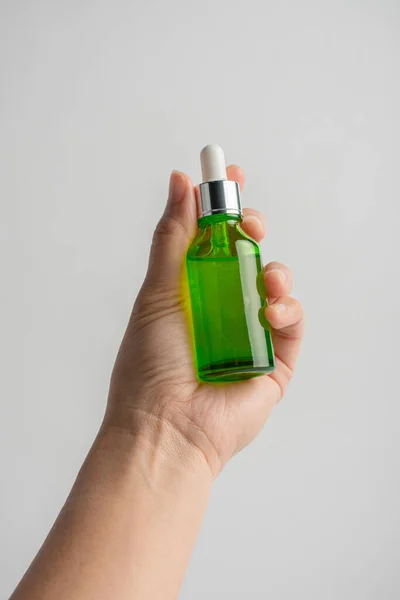 stock image Hand holding up a green glass dropper bottle on white background