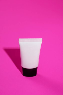 Krem veya losyon için plastik beyaz tüp. Pembe arka planda cilt bakımı veya güneş kremi kozmetiği.