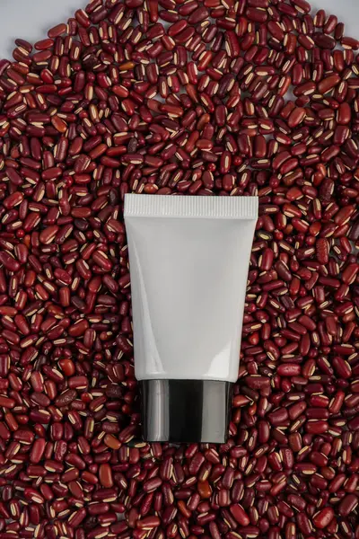 Plastic white tube for cream or lotion on red kidney beans background.