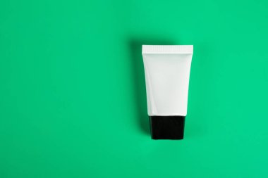 Krem veya losyon için plastik beyaz tüp. Yeşil arka planda cilt bakımı veya güneş kremi kozmetiği.