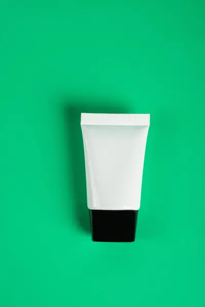 Plastic white tube for cream or lotion. Skin care or sunscreen cosmetic on green background.