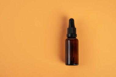 Krema arka planında koyu kehribar camından yapılmış kozmetik şişeler.