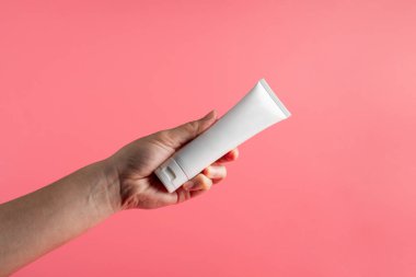 Krem veya losyon için plastik beyaz tüp. Cilt bakımı ya da pembe arka planda eli olan güneş kremi kozmetiği.