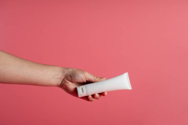 Krem veya losyon için plastik beyaz tüp. Cilt bakımı ya da pembe arka planda eli olan güneş kremi kozmetiği.