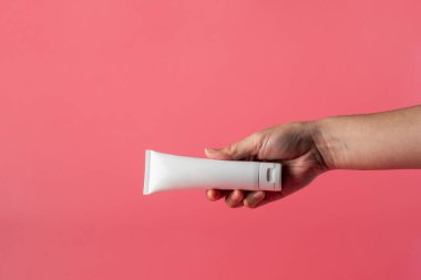 Krem veya losyon için plastik beyaz tüp. Cilt bakımı ya da pembe arka planda eli olan güneş kremi kozmetiği.
