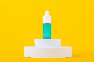 Mavi cam kozmetik şişesi, cilt bakımı veya sarı arka planda şık dekorları olan güneş kremi..