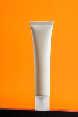  Turuncu arka planda nemlendirmek için kozmetik ürünü içeren boş bir tüp.
