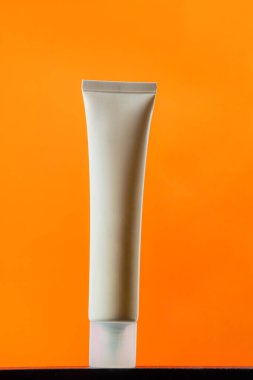  Turuncu arka planda nemlendirmek için kozmetik ürünü içeren boş bir tüp.