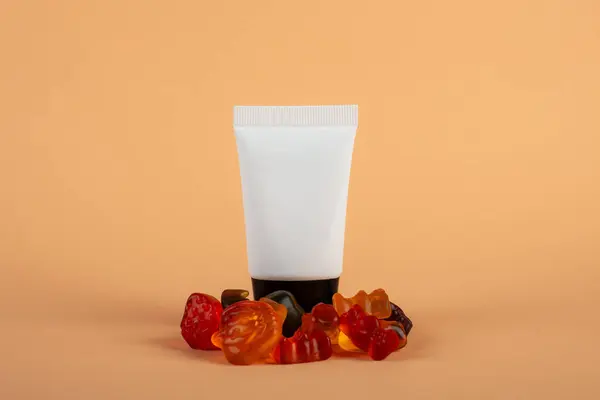 Krem veya losyon için plastik beyaz tüp. Cilt bakımı ya da güneş kremi kozmetik ürünleri ve krem arkaplanda meyveli jelibon..