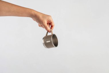 Eldeki paslanmaz çelik bardak beyaz arka planda izole edilmiş.