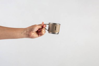 Eldeki paslanmaz çelik bardak beyaz arka planda izole edilmiş.