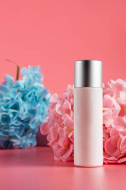 Krem veya losyon için plastik beyaz tüp. Cilt bakımı ya da pembe arka planda sahte çiçekli güneş kremi kozmetiği.