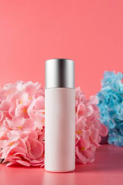 Krem veya losyon için plastik beyaz tüp. Cilt bakımı ya da pembe arka planda sahte çiçekli güneş kremi kozmetiği.