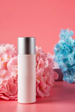 Krem veya losyon için plastik beyaz tüp. Cilt bakımı ya da pembe arka planda sahte çiçekli güneş kremi kozmetiği.