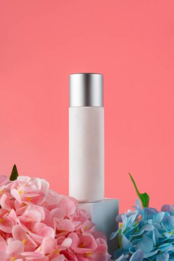 Krem veya losyon için plastik beyaz tüp. Cilt bakımı ya da pembe arka planda sahte çiçekli güneş kremi kozmetiği.