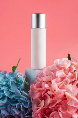 Krem veya losyon için plastik beyaz tüp. Cilt bakımı ya da pembe arka planda sahte çiçekli güneş kremi kozmetiği.