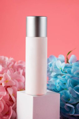 Krem veya losyon için plastik beyaz tüp. Cilt bakımı ya da pembe arka planda sahte çiçekli güneş kremi kozmetiği.