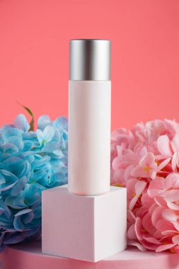 Krem veya losyon için plastik beyaz tüp. Cilt bakımı ya da pembe arka planda sahte çiçekli güneş kremi kozmetiği.