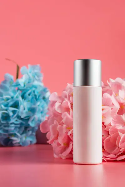 Krem veya losyon için plastik beyaz tüp. Cilt bakımı ya da pembe arka planda sahte çiçekli güneş kremi kozmetiği.