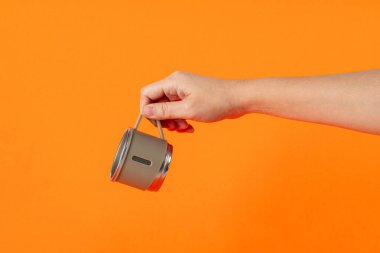 Eldeki paslanmaz çelik bardak turuncu arka planda izole edilmiş.