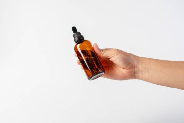 Siyah kehribar camdan yapılmış kozmetik şişeleri ve beyaz arka planda el.