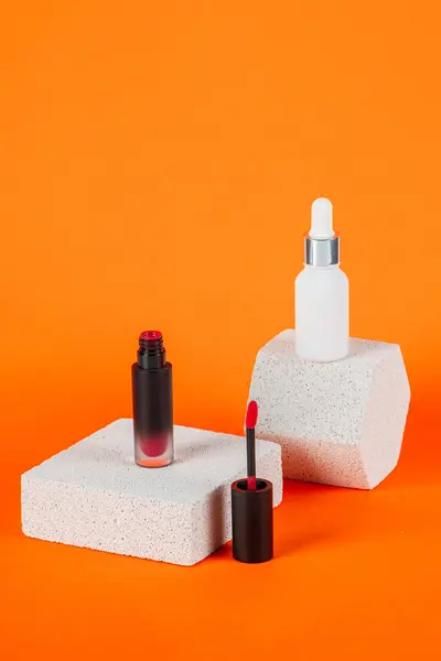 Siyah, boş, ince bir tüp. Rimel, dudak parlatıcısı, jöle, göz kalemi, yağ vs. Turuncu arka planda şık dekorları olan kozmetik paketler..