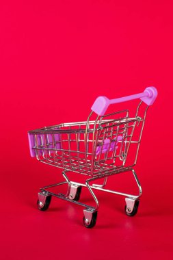 Boş oyuncak metal süpermarket alışveriş arabasını kırmızı arka planda fotokopi alanı ile kapat,